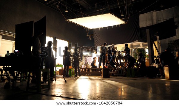 Behind the scenes or the making of film video production\
and movie crew team working in silhouette of camera and equipment\
set in studio. 