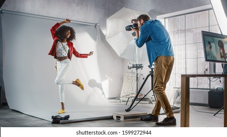 Behind The Scenes On Photo Shoot: Beautiful Black Model Poses For A Photographer, He Takes Photos With Professional Camera. Stylish Fashion Magazine Photoshoot Done With Pro Equipment In A Studio