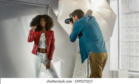 Behind The Scenes On Photo Shoot: Beautiful Black Model Posing For A Photographer, He Takes Photos With Professional Camera. Stylish Fashion Magazine Photoshoot Done With Pro Equipment In A Studio