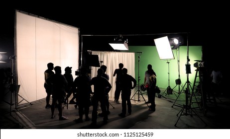 Behind The Scenes Of TV Commercial Movie Film Or Video Shooting Production Which Crew Team And Camera Man Setting Up Green Screen For Chroma Key Technique In Big Studio.