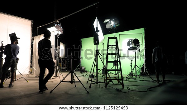 Behind the scenes of TV\
commercial movie film or video shooting production which crew team\
and camera man setting up green screen for chroma key technique in\
big studio.