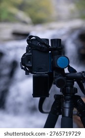 Behind the scenes view of a camera mounted on a tripod capturing a waterfall with long exposure technique in a natural forest environment.