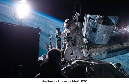 Behind The Scenes Of Virtual Production Shot - Film Crew Working With Caucasian Female Astronaut Stuntwoman In A Spacesuit Hanging On A Wires Against Huge LED Screen. Some Elements Furnished By NASA