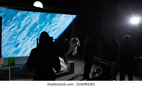 Behind The Scenes Of Virtual Production Shot - Film Crew Working With Caucasian Female Astronaut Stuntwoman In A Spacesuit Hanging On A Wires Against Huge LED Screen. Some Elements Furnished By NASA