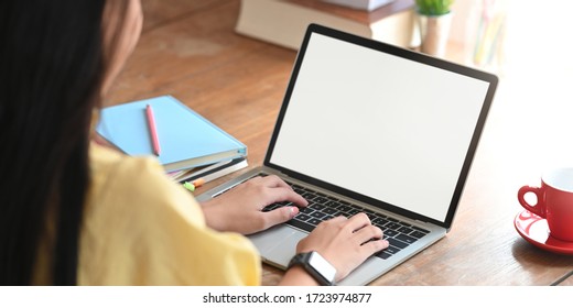 Behind shot of beautiful woman working as accountant while sitting and working with white blank screen computer laptop at the wooden working desk that surrounded by coffee cup and stack of books.