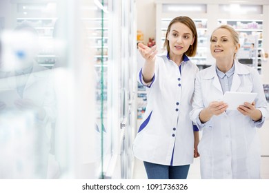 Behind showcase. Thoughtful female pharmacists standing and looking at showcase - Powered by Shutterstock