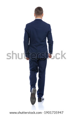 behind view of elegant young man in navy blue suit walking isolated on white background in studio