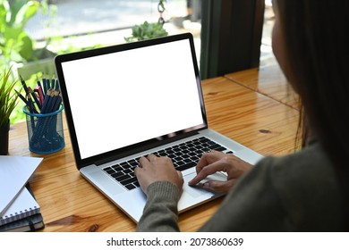 Behind View Of A Young Woman Using A White Blank Screen Computer Laptop At The Wooden Working Desk.