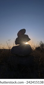 Behold the breathtaking sight of a stack of rocks standing tall and proud as the sun sets behind them, casting a warm and golden glow across the landscape.