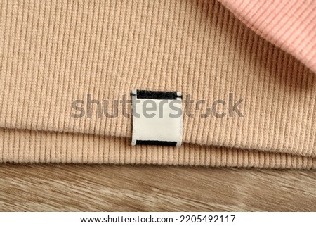 Beige apparel with blank clothing label on wooden table, top view