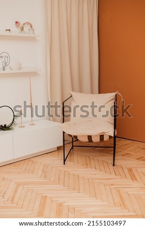A beige armchair stands in a bright interior near an orange wall