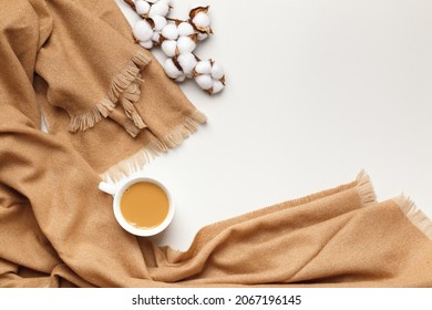 Beige cashmere scarf with a cup of coffee and a sprig of cotton on a light gray background. Flat lay top view copy space. Autumn winter coziness concept