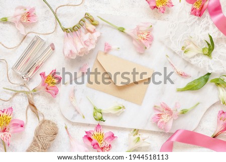Beige envelope on a white table between pink flowers  top view