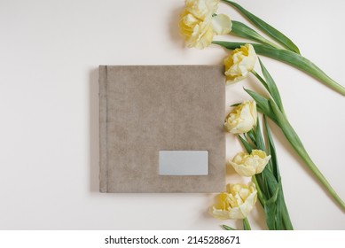 Beige Family Or Wedding Photo Book And Tulip Flowers Lie On A Light Beige Background. Fond Memories In Photographs For Memory