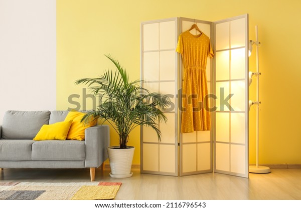 Beige folding screen with dress near yellow wall in\
living room