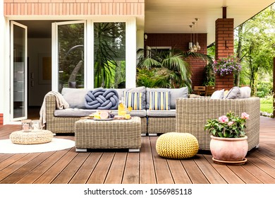 Beige garden furniture with striped pillows on a wooden terrace with pink flowers and poufs