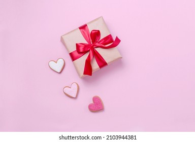 Beige gift box with a beautiful red bow on a pink flatlay background. A gift with a satin ribbon and hearts with a place for text. Beautiful concept for Valentine's Day