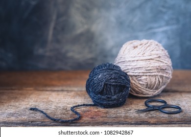Beige and Grey yarn balls with scissors on a rustic wooden background, toned