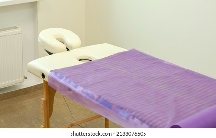 Beige massage table covered with a disposable sheet. Massage table with headrest in a massage room - Powered by Shutterstock