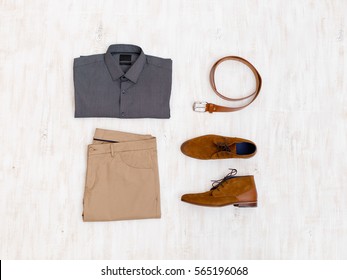 Beige Pants, Grey Shirt, Brown Suede Shoes And Leather Belt. Overhead View Of Men's Casual Outfit On White Wooden Background. Flat Lay, Top View.