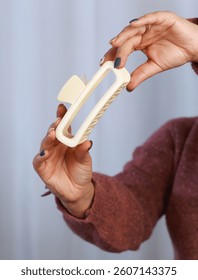 Beige rectangular claw clip held in hand, modern hair accessory with minimalist design, close-up product photo for catalog, styling, editorial and ecommerce stock use, neutral color palette and fashio