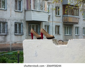 Beige Red Old Women Shoes With High Heels In Foreground Exhibited Free Of Charge For Needy Homeless Poor People Near Trash On Concrete Slab Stand. Residential Area Project Apartment Back Court Yard.