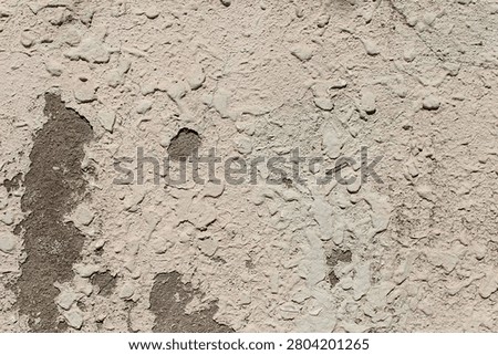 Beige rough plaster wall with a small hole and natural imperfections.