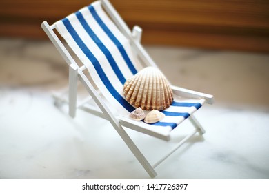 Beige Shells Of Various Sizes Lie On A Little Vintage Decoration Striped Beach Chair, Side View