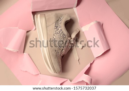 beige sneakers on pink paper background with torn hole for copy space. Top view. Minimalism fashion concept