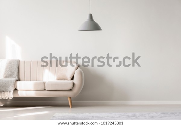 Beige sofa against white, empty
wall with copy space in simple living room interior with
lamp