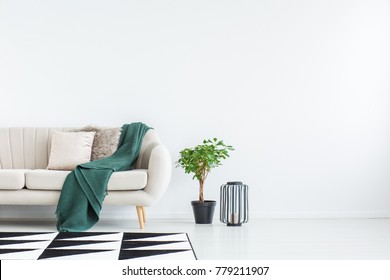 Beige Sofa With Green Blanket And Cushions Standing Against White, Empty Wall In Minimalistic Living Room