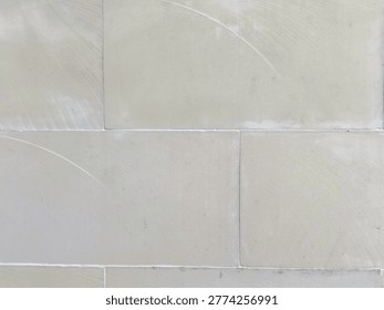 Beige stone wall texture serving as a neutral background with subtle tile seams and plastered surface. Minimal architectural detail creates a calm, modern backdrop for design, editorial, and construction use
