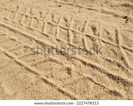 Beige surface of sand with a wavy track from the tires of an already passed car (diagonal, top view, texture).
