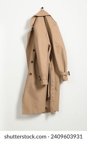 Beige trench coat hanging on hook rack on white wall