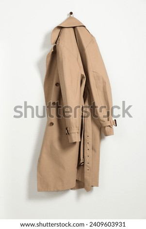 Beige trench coat hanging on hook rack on white wall