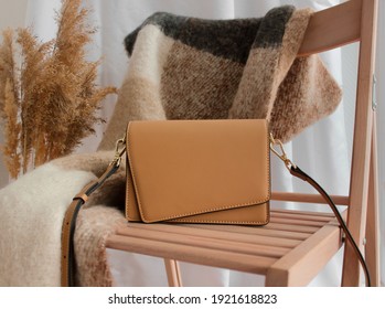 Beige trendy women's bag, against the background of a beige scarf accessory, lying on a chair. Photos for studios, showrooms, boutiques and shops selling women's accessories.
