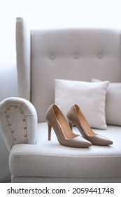 Beige wedding shoes on white sofa close up. Luxury pair of highheel female shoes on a couch. Female elegant shoes fashion style.