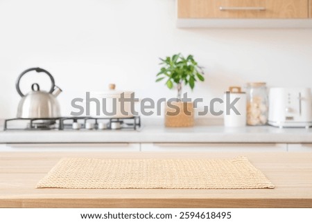 Beige woven rectangular placemat on wooden table top over blurred kitchen room gas stove counter background