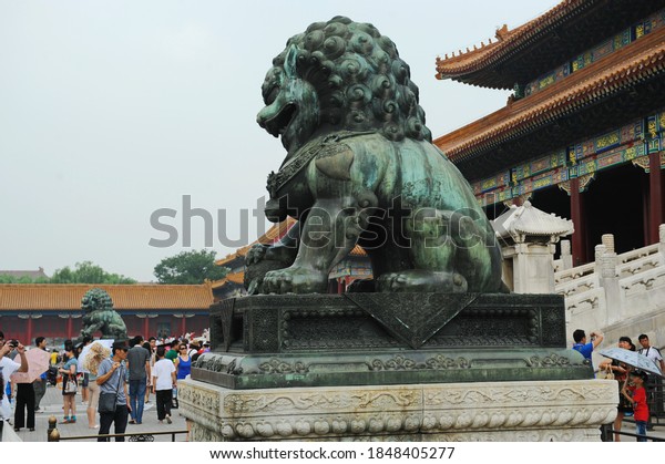 Beijing / China - 08.06.2012 : Statue of the\
heavenly lion among the Palace structures in the forbidden city,\
where tourists walk.