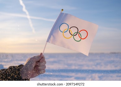 Beijing, China - 10.10.2021 - The Olympic flag, small in hand, flutters against the backdrop of snow and trees Concept for Winter Olympic Games 2022.