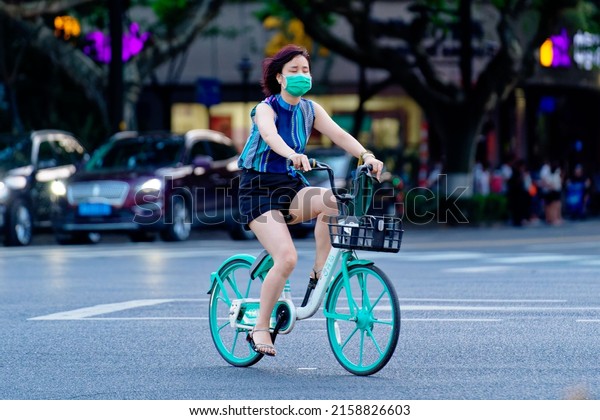 BEIJING, CHINA - Jul 21,\
2021: A close-up shot of a girl with a mask riding a bike on the\
streets of Beijing