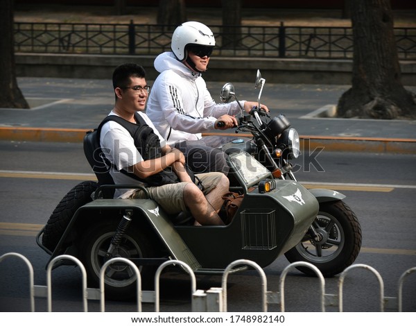 Beijing, China - June 27,\
2019: A motorcyclists drives a bike and a sidecar along a city\
centre street.