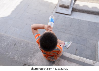 Beijing, China - MAY 8, 2017: A Chinese Boy Drinking Water From A Plastic Bottle To Prevent Himself From Dehydration On A High Temperature Day, And Resting Under The Shadow Of Building 