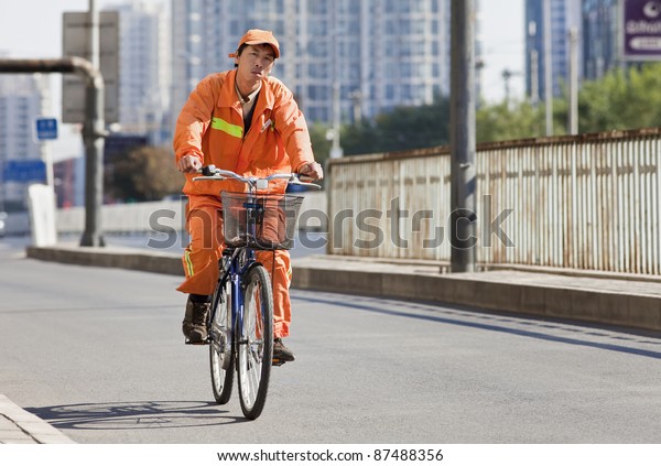 BEIJING - OCT. 25:\
Worker in orange cycles in Beijing, Oct. 25, 2011. From 1995 to\
2005, China\'s bike fleet declined by 35 percent and private car\
ownership more than\
doubled.