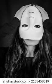 Being different even when wearing a mask - portrait of a young long-haired woman with a mask upside down and hands on her head - concept
