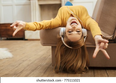 Being energetic. Pretty overjoyed young blond woman laughing and listening to music and wearing headphones while lying on the sofa and wearing a yellow sweater - Powered by Shutterstock