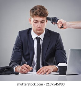 Being Forced To Sign The Papers. A Business Man Signing A Piece Of Paper With Someone Pointing A Gun At His Head.