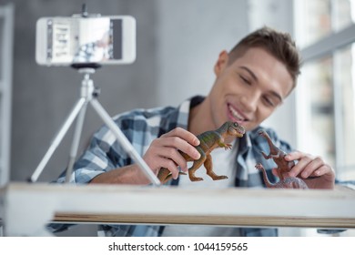 Being inspired. Nice cheerful smart well-built teenager smiling and holding a little dinosaur in his hand while making a video