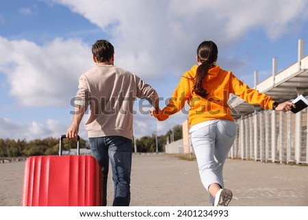 Being late. Couple with red suitcase running outdoors, back view