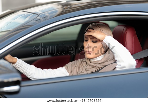 Being\
Late. Upset and tired muslim woman in hijab driving car in urban\
city, got stuck in traffic jam. Sad arabic lady in headscarf\
touching head, feeling anxiety, headache or\
stress.